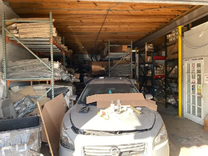 Cluttered auto body shop storage area with car.