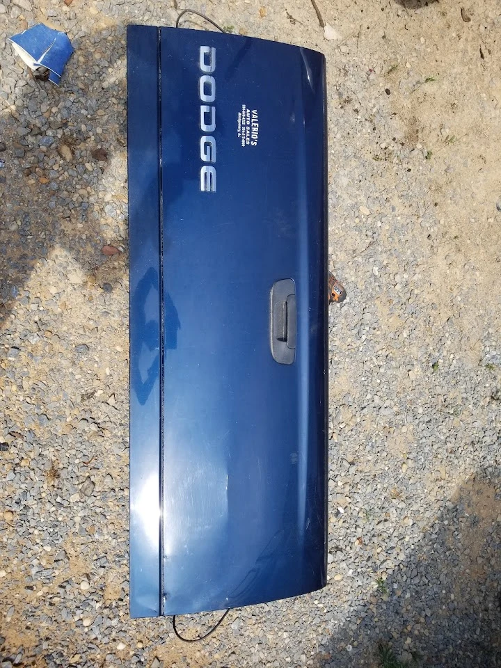 Dodge truck tailgate, blue, on a gravel surface.