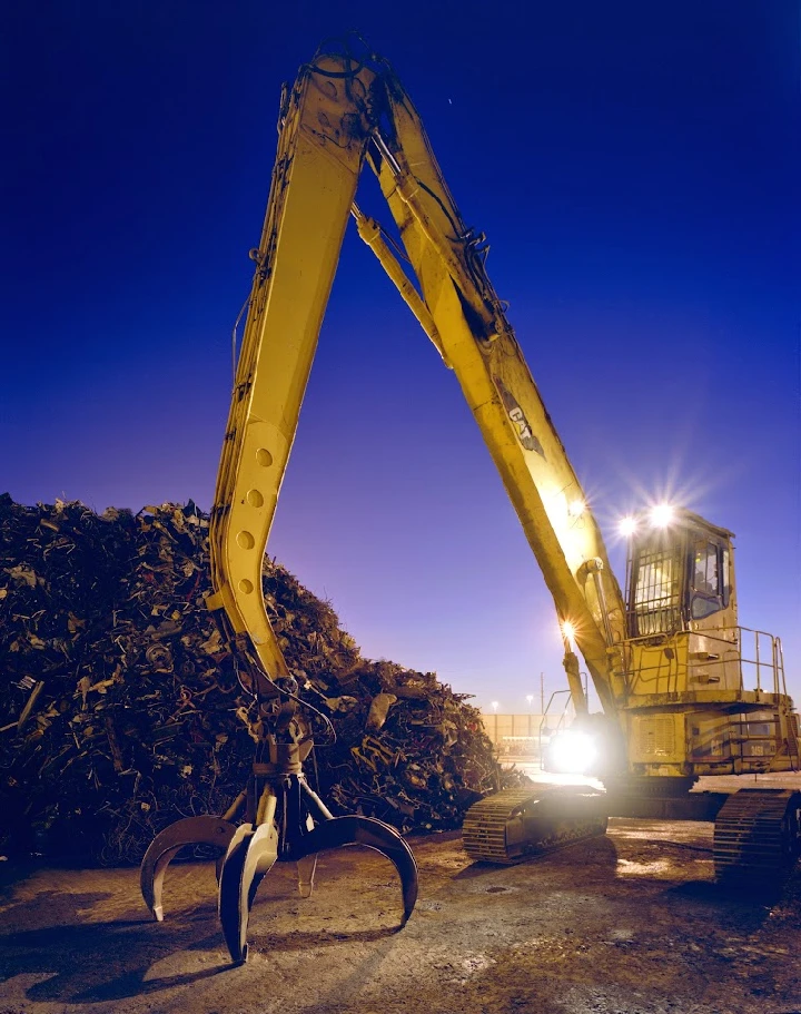 Excavator lifting metal scrap at twilight.