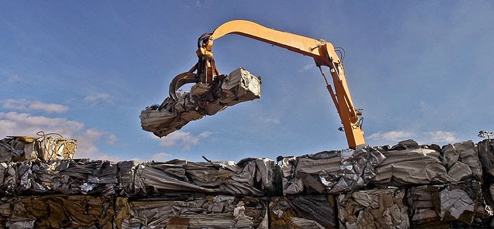 Excavator lifting scrap metal at recycling facility.