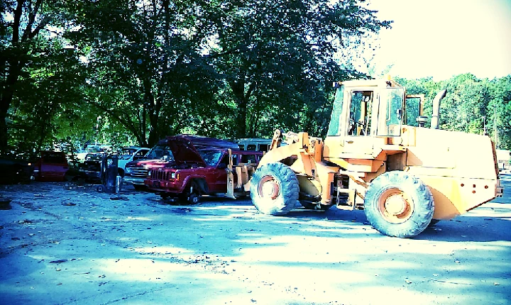 Heavy machinery in a salvage yard with vehicles.