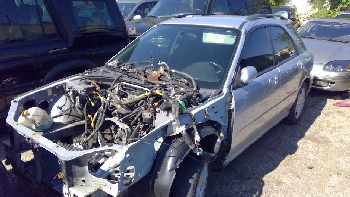 Junk car with missing engine parts at a lot.