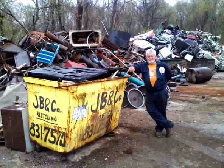 Man standing by a recycling dumpster in a scrapyard.