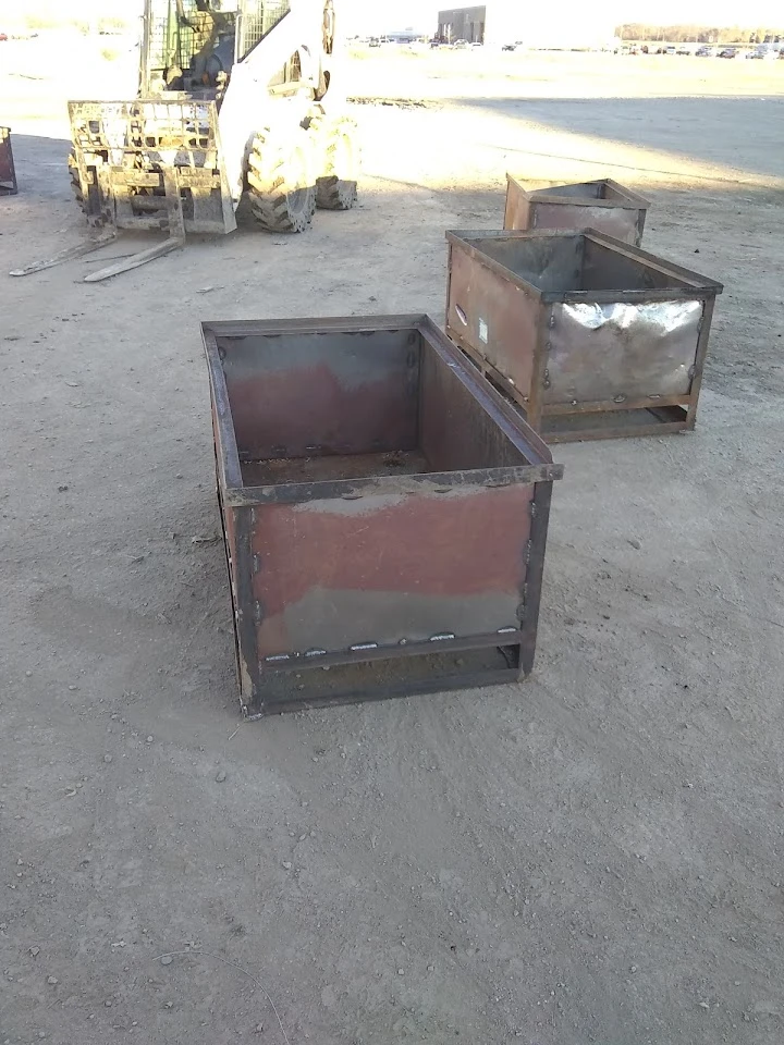 Metal recycling bins in a yard with machinery.