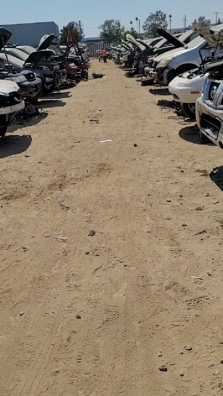 Row of cars in a junkyard with sandy path.