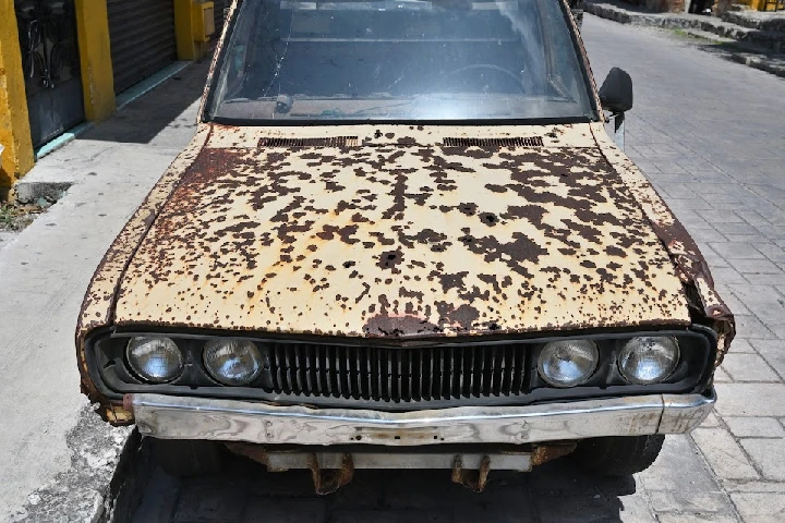 Rusty abandoned car in urban setting.