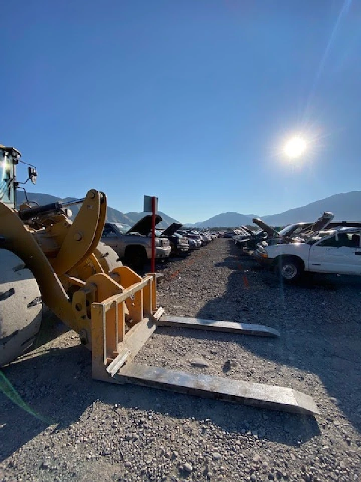 Sunlit salvage yard with vehicles and heavy machinery.