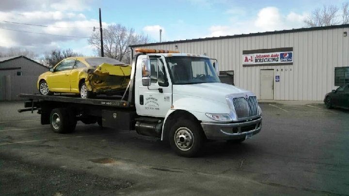 Tow truck with a yellow car at A-1 Johnson Auto Wrecking.