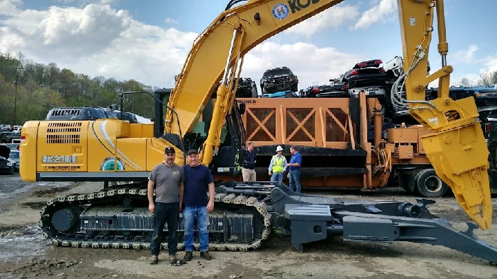 Two men stand near a large yellow excavator.