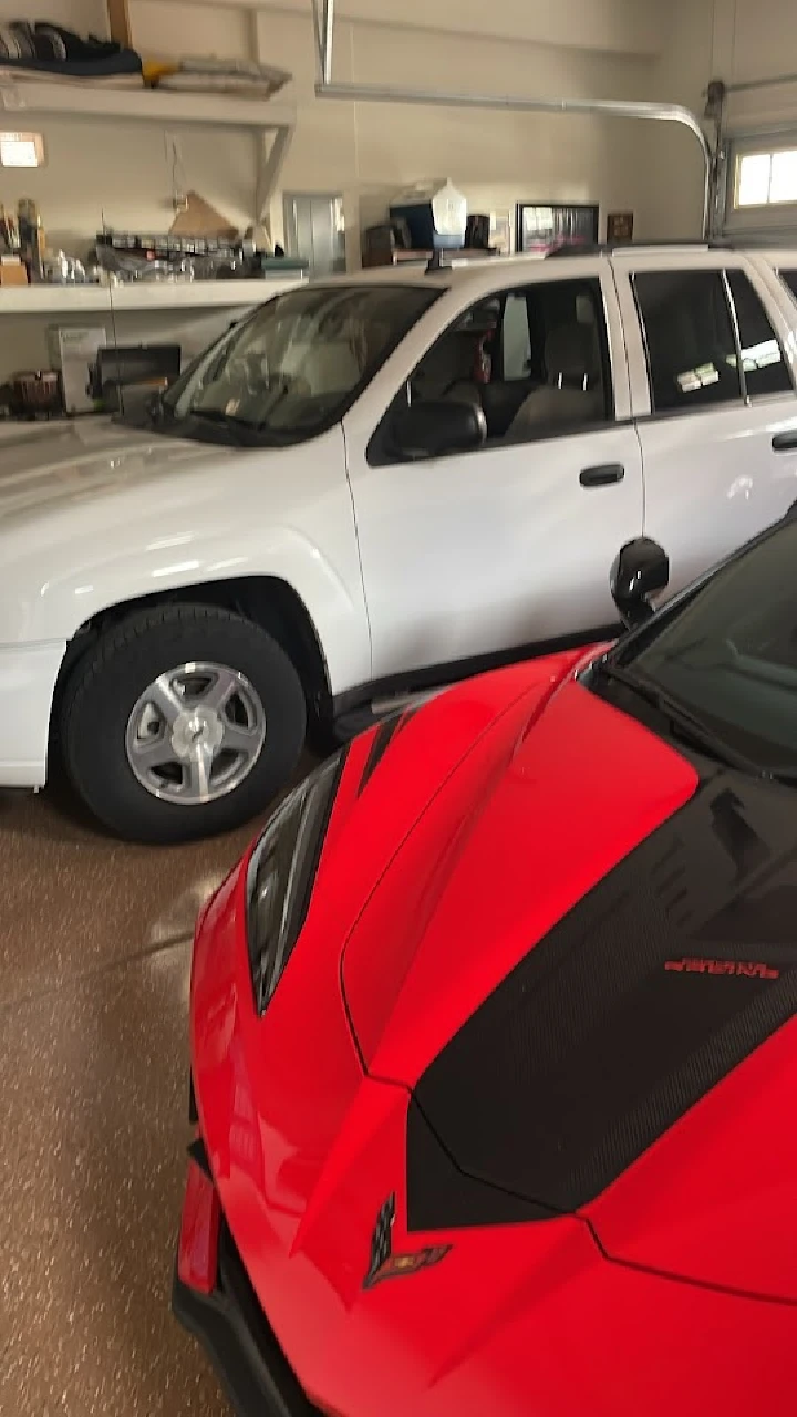 Two vehicles in a garage: a white SUV and red sports car.