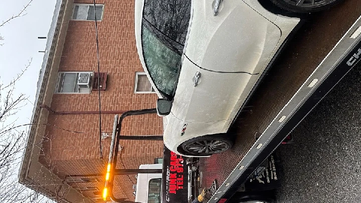 White car being towed by a truck in light rain.