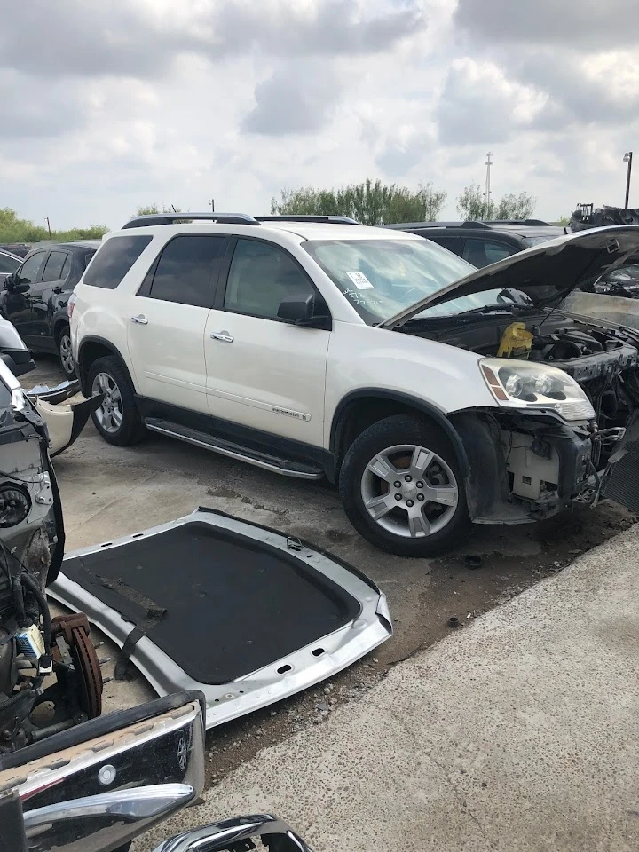 White SUV with open hood in auto parts yard.