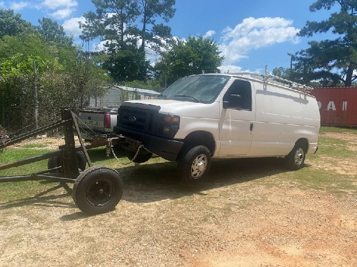 White van in a junkyard with trailer.