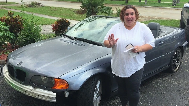 Woman smiling by a gray convertible car outdoors.