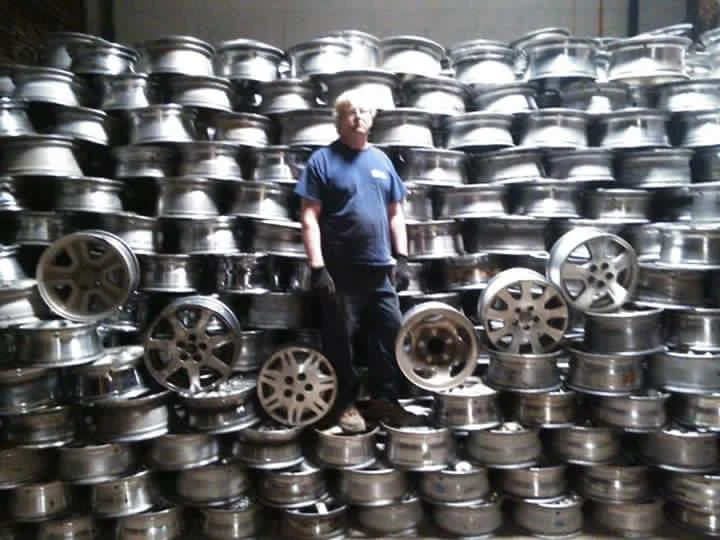 Worker stands among stacked automotive wheels.