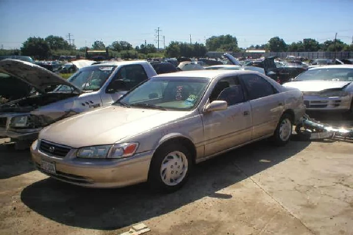 A gold sedan parked among junked cars in a salvage yard.