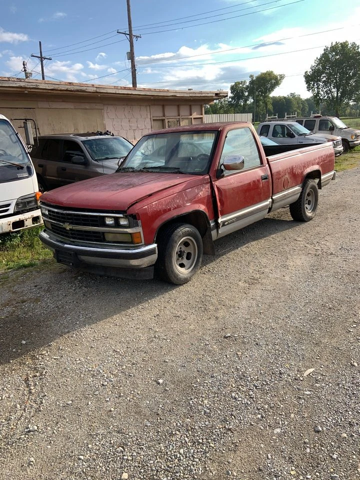 Abandoned red pickup truck at auto salvage yard.