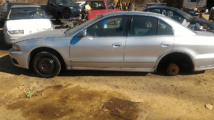 Abandoned silver car on a salvage yard lot.