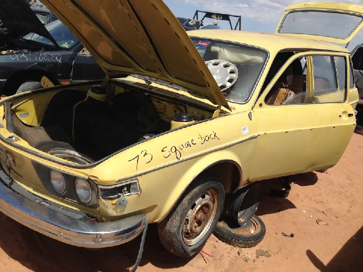 Abandoned yellow 1973 vehicle in junkyard.