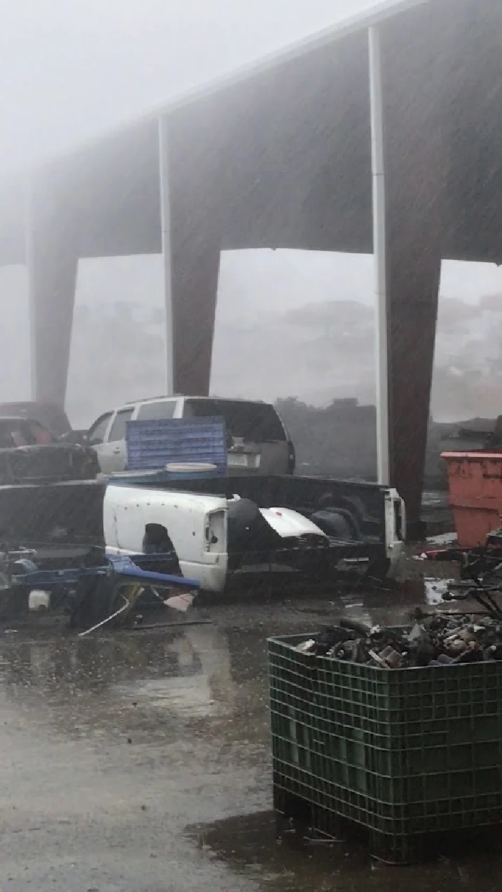 Auto parts yard in rainy weather, various vehicles visible.