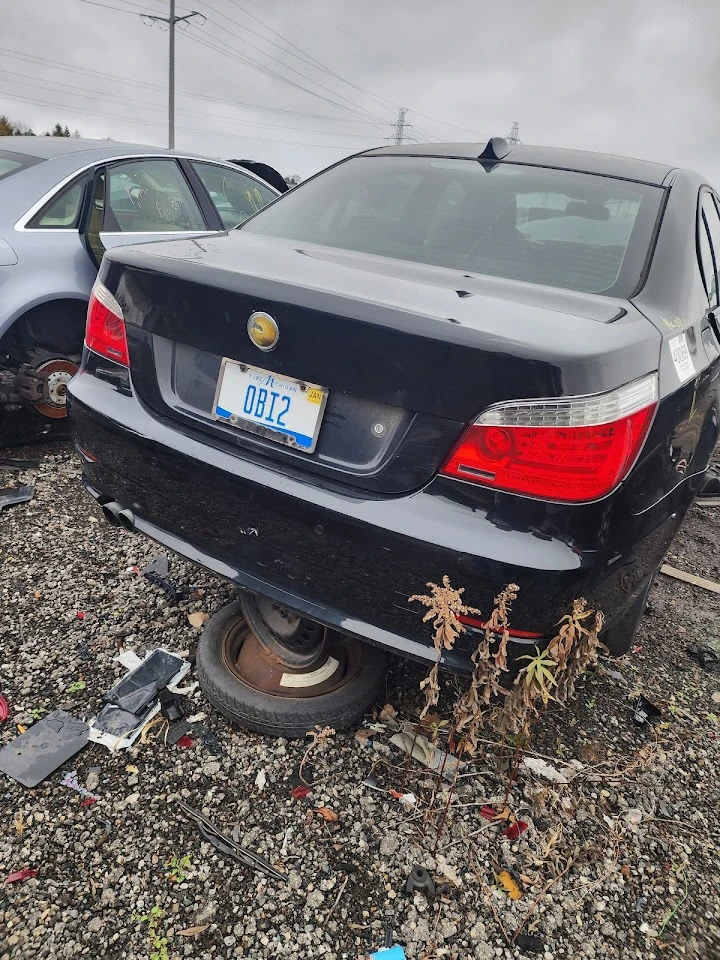 Black car in junkyard on a rusted wheel.