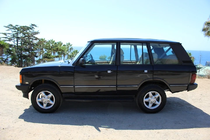 Black Land Rover parked by the ocean. Sunny day.