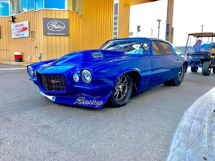 Blue racing car parked outside a dealership.