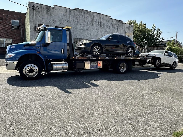 Blue tow truck carrying two cars on a street.