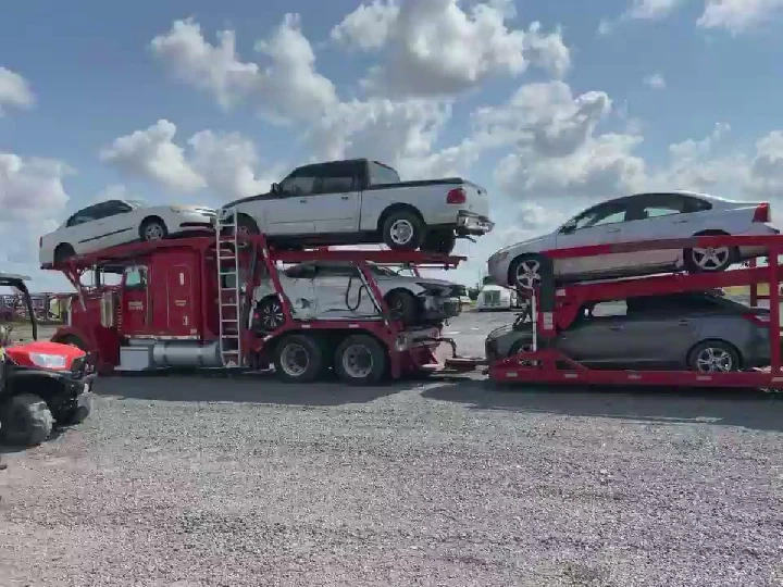 Cars stacked on a red truck against a blue sky.