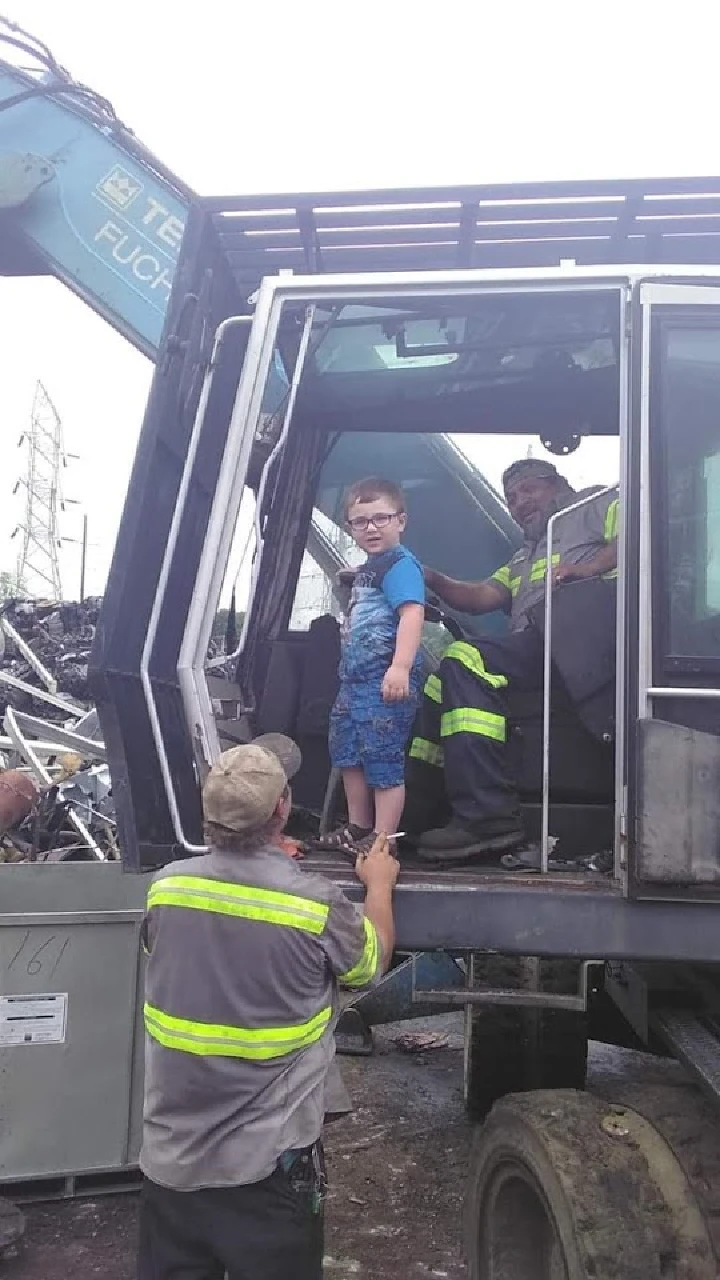 Child exploring a recycling truck with workers.