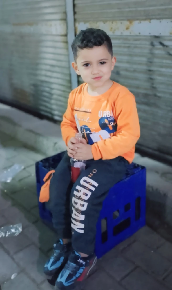 Child sitting on a crate, wearing orange shirt.