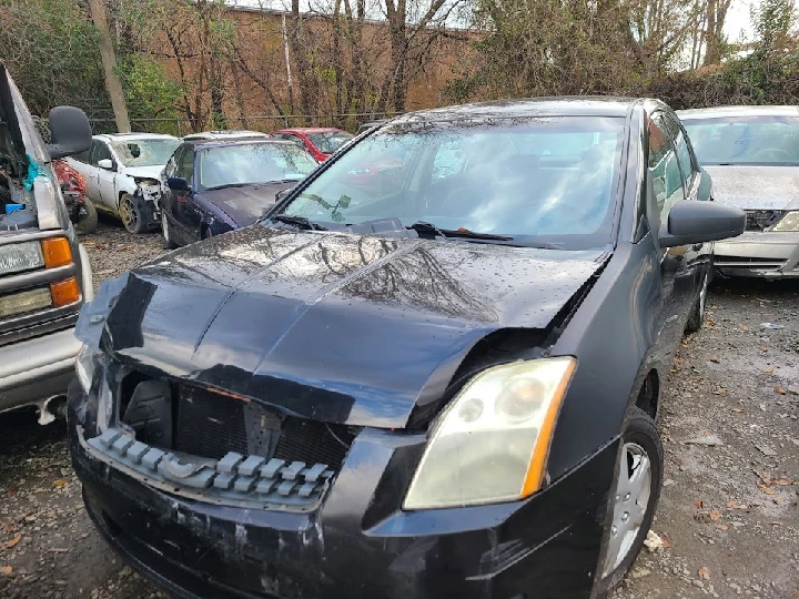 Damaged black car in a junkyard for cash offers.