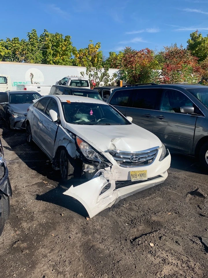 Damaged white car in auto recycling yard.