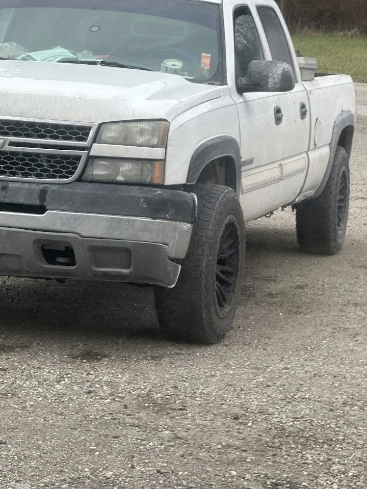 Dirty white truck parked on gravel ground.