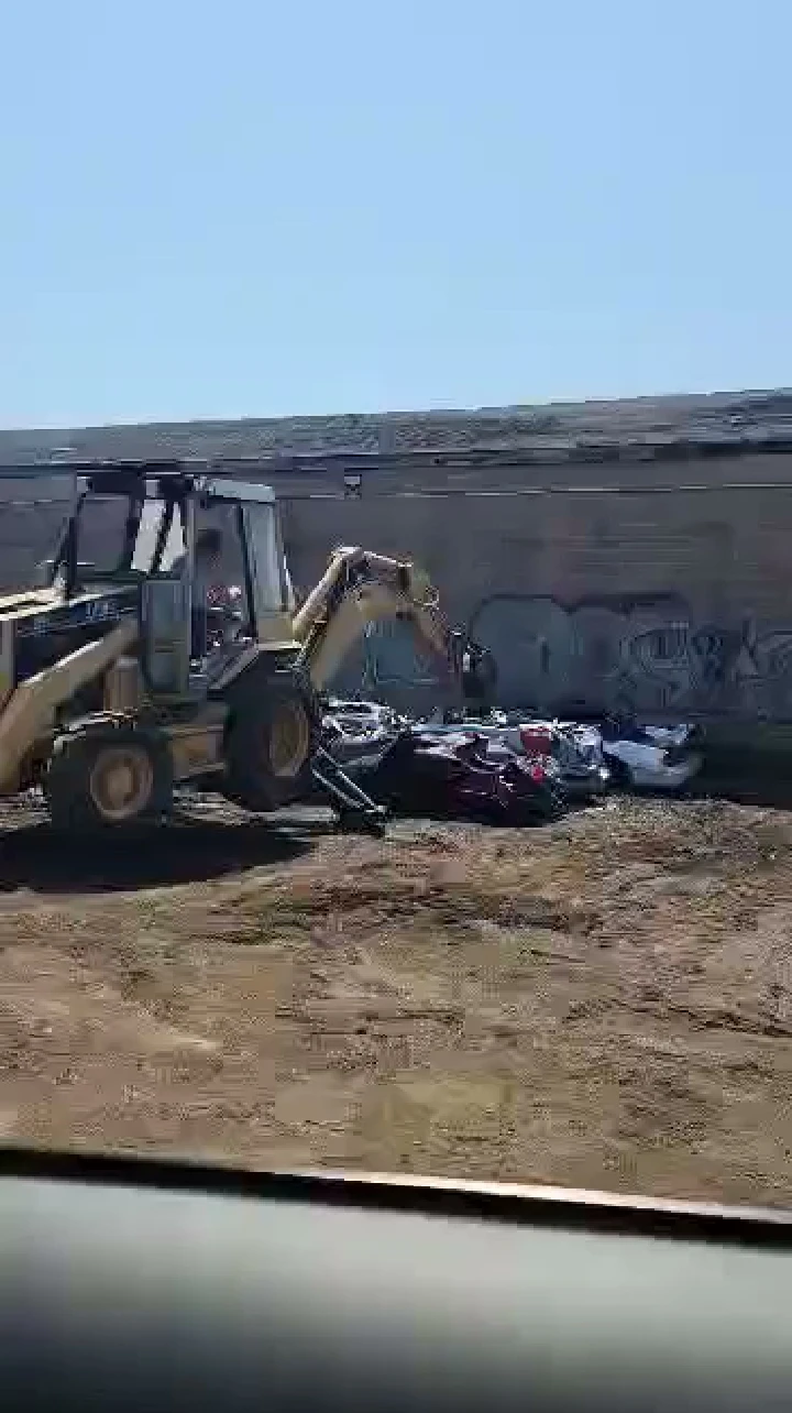 Excavator removing scrap vehicles at towing yard.