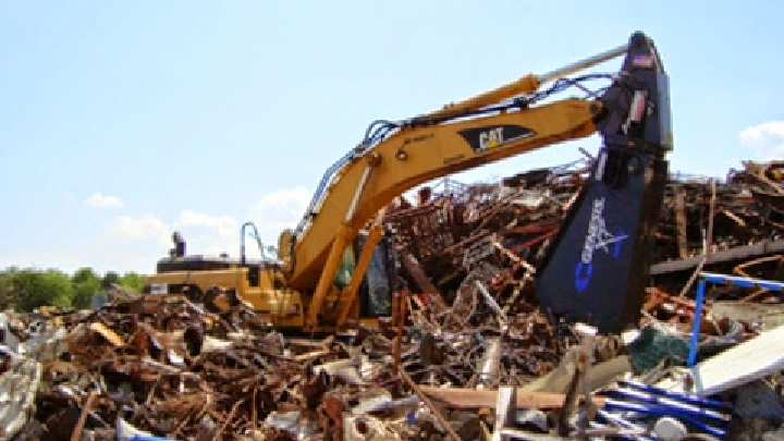 Excavator sorting scrap metal at recycling facility.