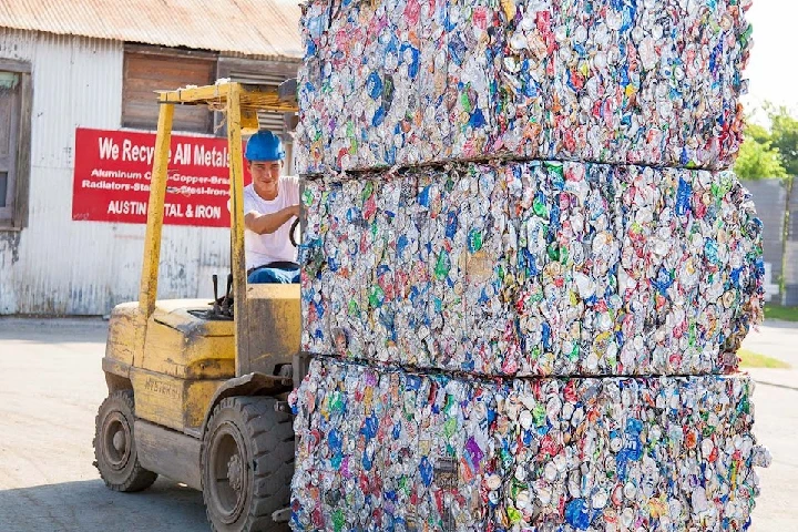 Forklift moving stacked cans at recycling facility.