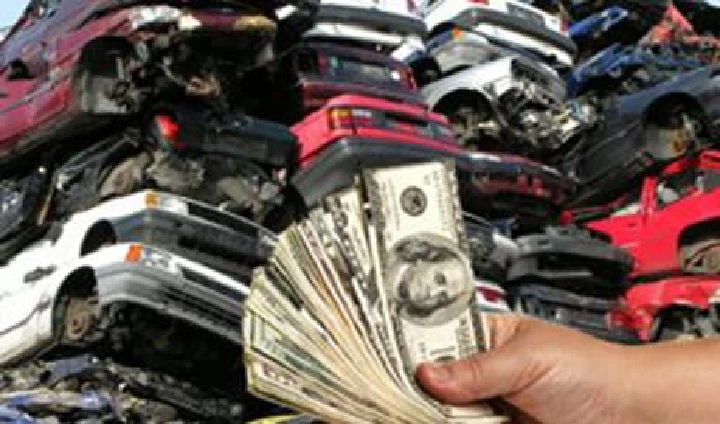 Hand holding cash in front of stacked junk cars.