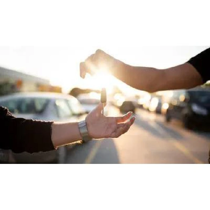 Hands exchanging car keys in sunlight.