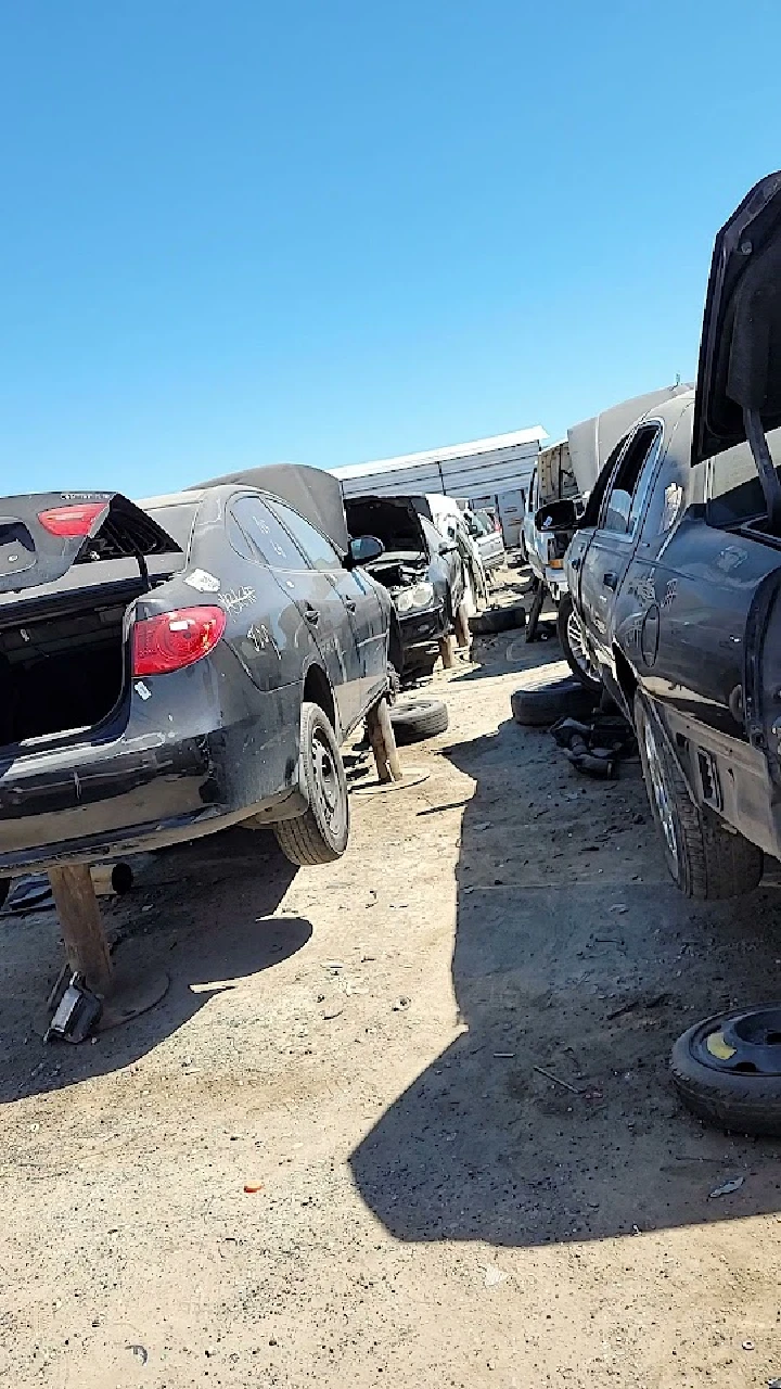 Junkyard with cars and parts under a clear sky.