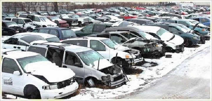 Junkyard with various wrecked vehicles in snow.