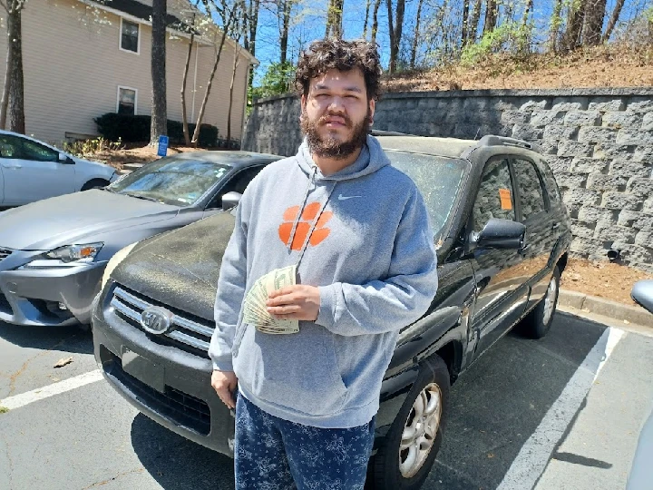 Man holding cash next to a junk car.