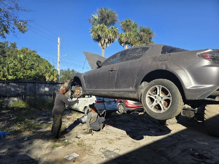 Mechanics working on a raised vehicle at a salvage yard.