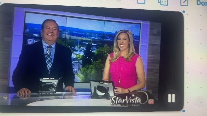 News anchors smiling on set during a broadcast.