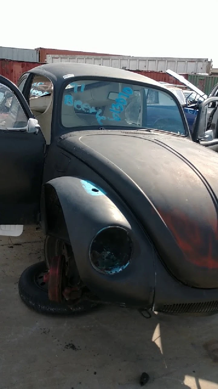 Old black Volkswagen Beetle in a junkyard.