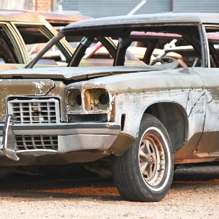 Old, rusty car in a junkyard setting.