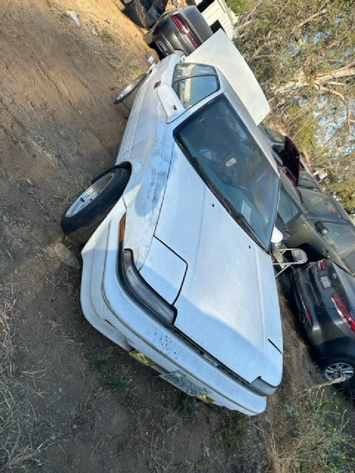 Old white car in a junkyard setting.