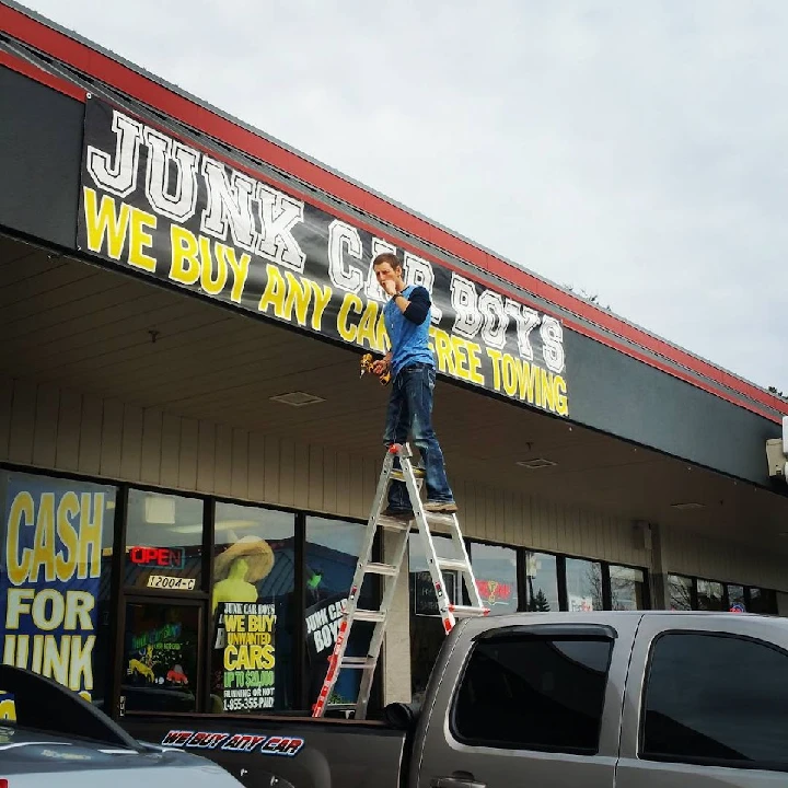 Person on ladder adjusting a sign for Junk Car Boys.