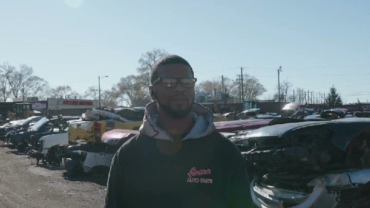 Person standing among used cars at Acme Auto Parts.