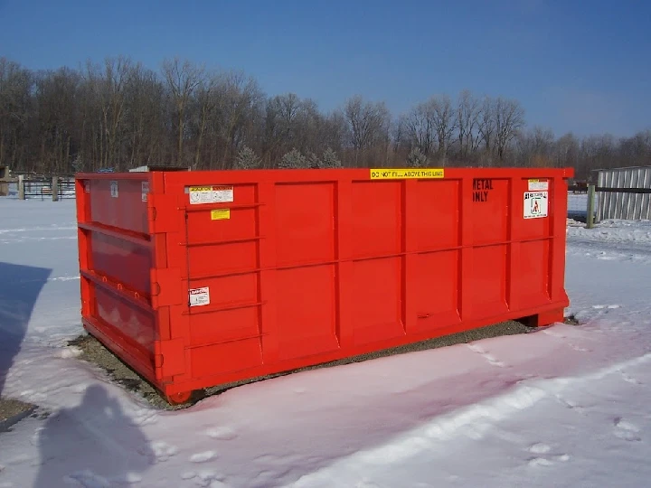 Red dumpster for metal recycling, snowy background.